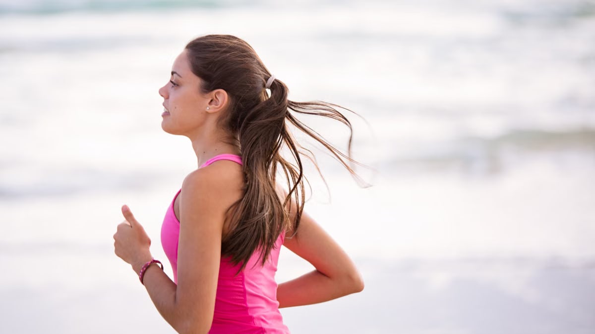 Side view of a young woman jogging on a beach wearing pink active wear.